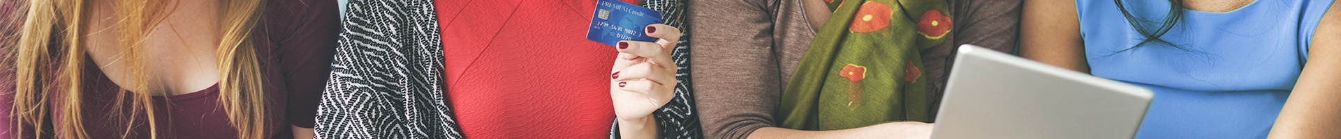 Tax Free - Mujeres sentadas en el sofa de casa sonriendo con tarjetas en la mano mirando la tablet