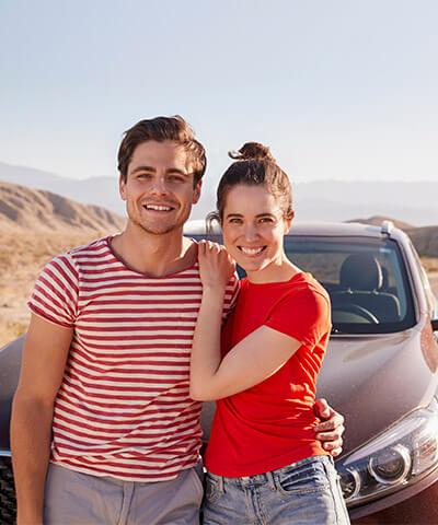 Seguro del Automóvil - Pareja joven abrazados junto a su coche al lado de la carretera en el desierto